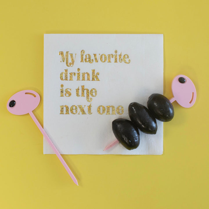 Pink fancy acrylic cocktail picks with rhinestone next to a napkin that says "My favorite drink is the next one"