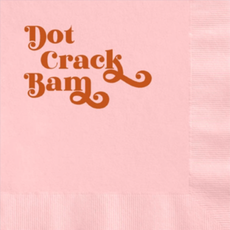 Pink napkin with decorative text 'Dot Crack Bam' in brown on a pink background