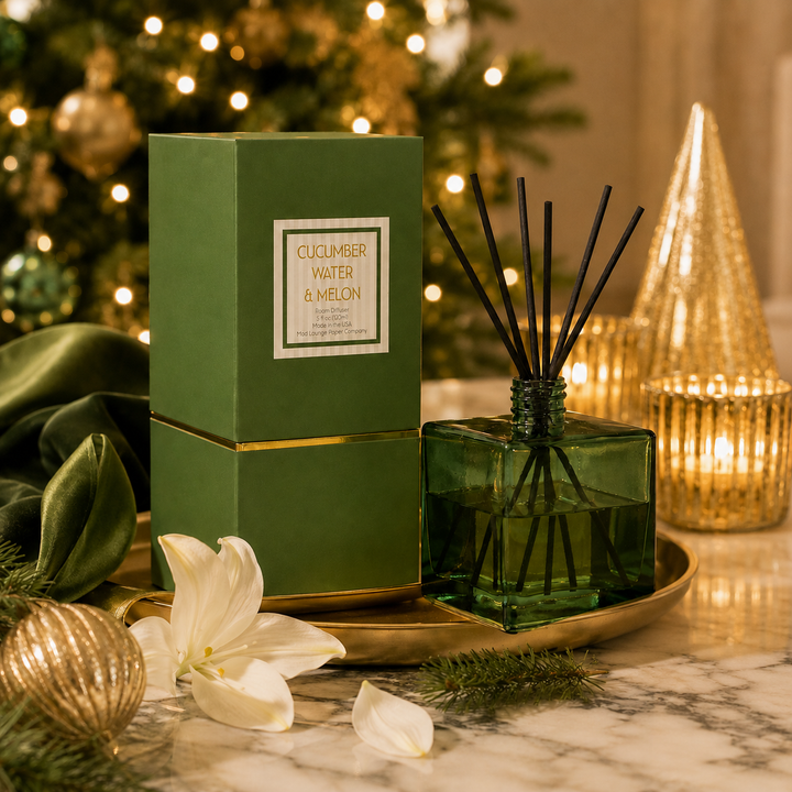 A reed diffuser set with a green glass bottle, black reeds, and a matching green box labeled &