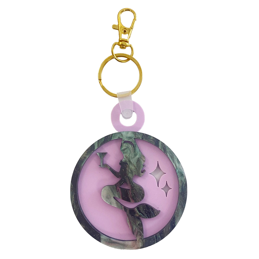 A round acrylic keychain with a vintage mermaid design, featuring galaxy glitter on a matte lilac background, and a gold plated lobster claw for attachment.