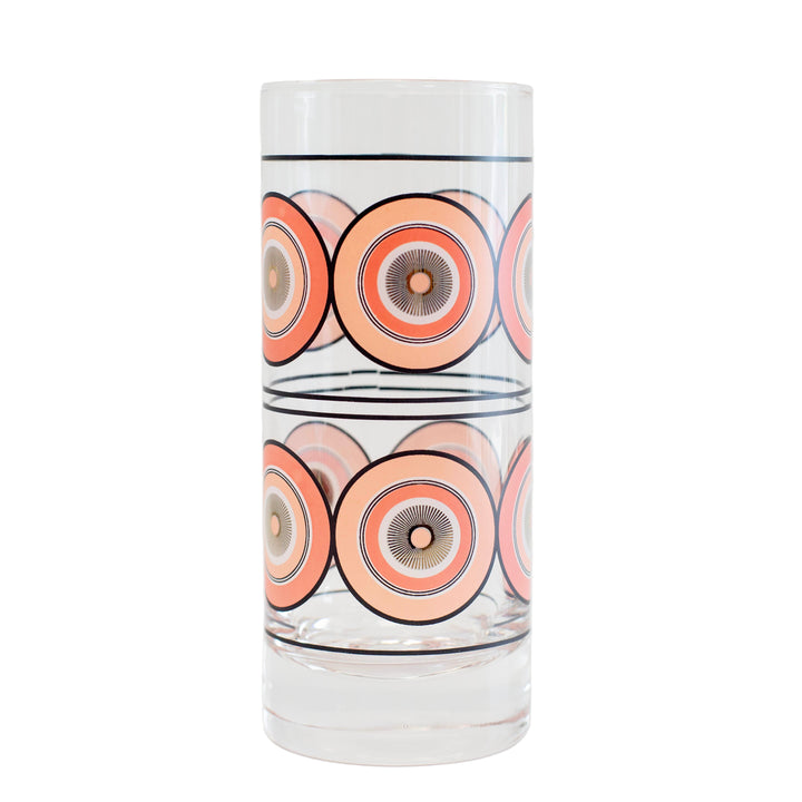 A clear highball collins glass with a mid century modern geometric pink circle and gold starburst pattern.