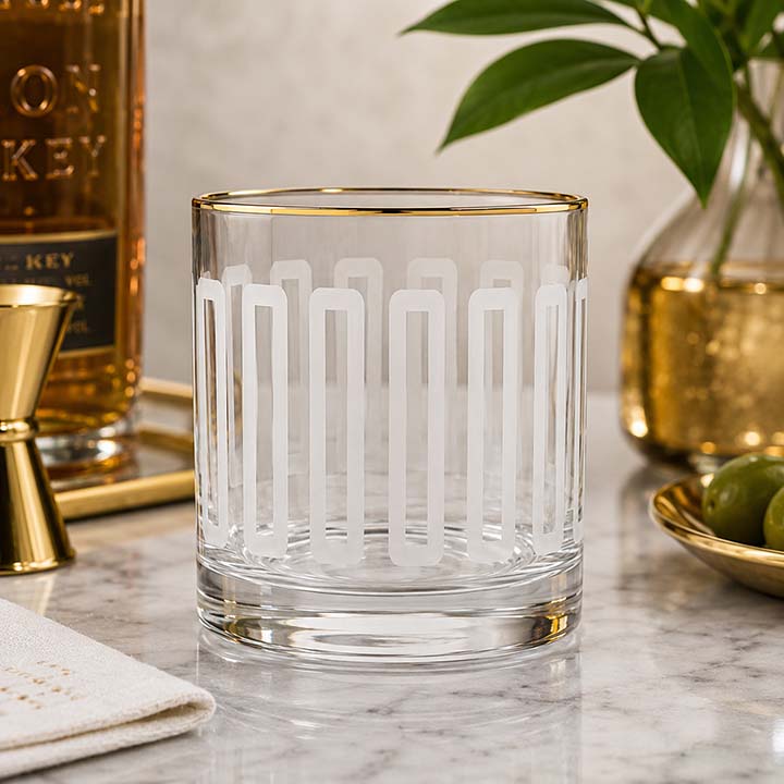Frosted lead-free crystal whiskey glass featuring a white geometric pattern, metallic gold rim, and weighted base on a clear background.